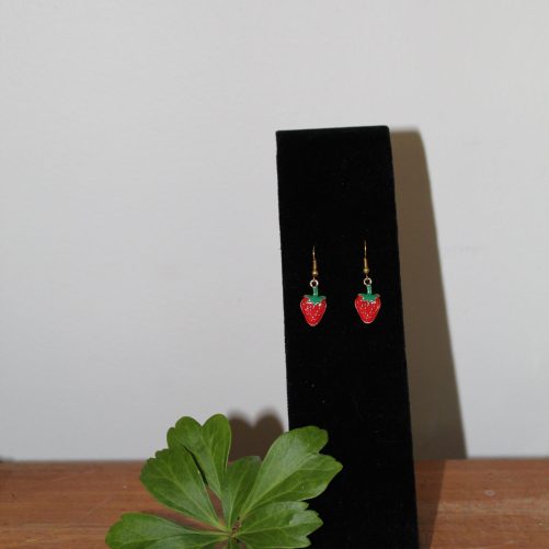 Strawberry dangle earrings on a black stand with a sprig of Japanese pachysandra.